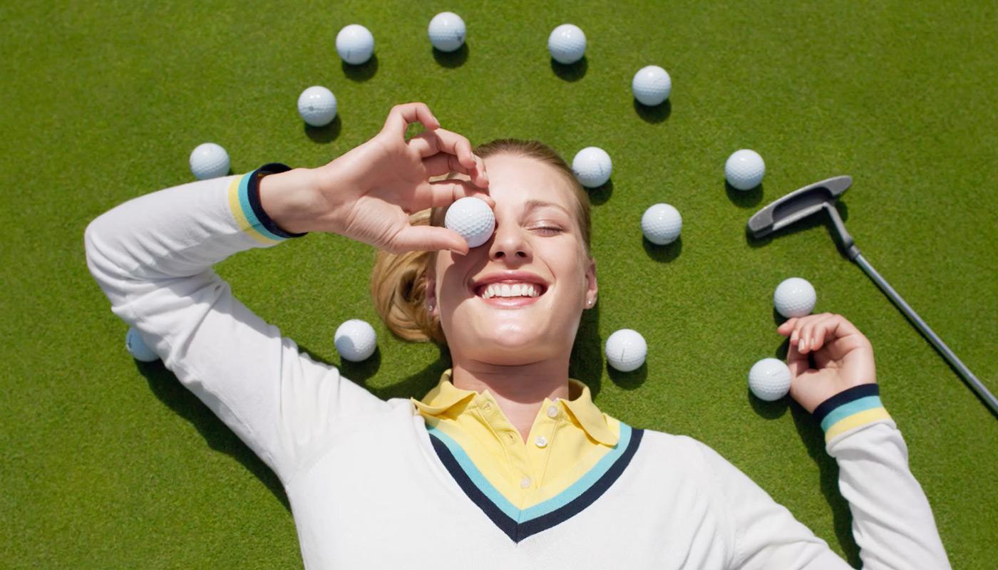 Happy girl laughing on the ground surrounded by golf balls.
